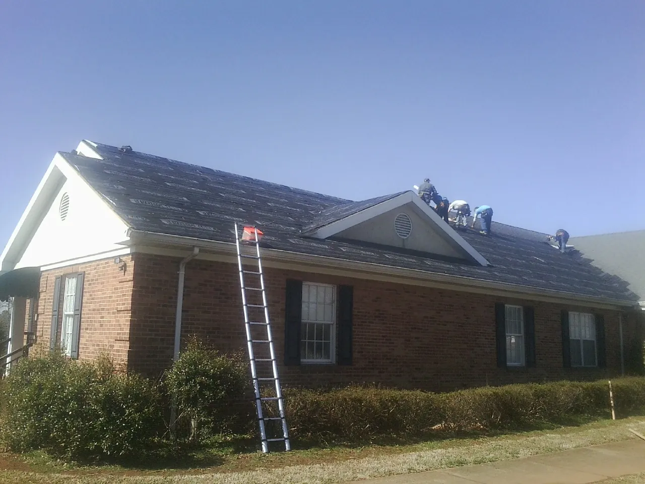 Crew tearing shingles off a brick ranch roof with a ladder set — Emergency Roof Repair work by our crew in Pylesville