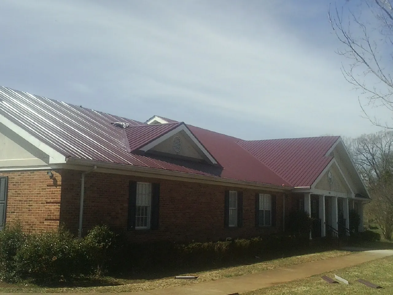 Red metal roof with gabled entries on a long brick building, from a Hail Damage Roof Repair job in Pylesville