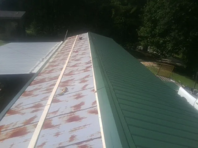 Old rusted panels beside newly installed green metal roofing — Wind Damage Roof Repair by Roofing Brothers in Pylesville