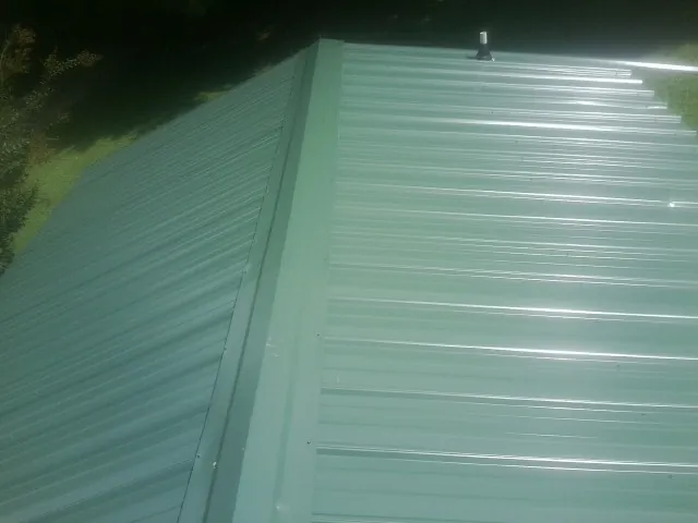 New green metal panels meeting at the ridge of a roof — Flat Roof Repair work by our crew in Pylesville