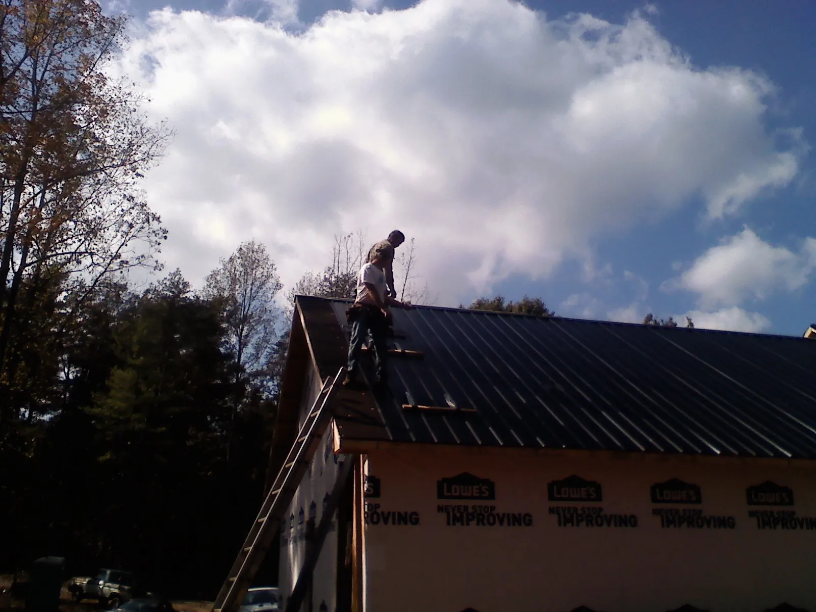 Roofer fastening dark metal panels high against a cloudy sky, from a Roof Inspection job in Pylesville